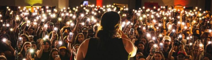 Silhouette of a singer on stage looking out towards the crowd who are holding their phone torches up.