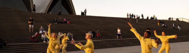 A group of dancers in yello tracksuits dancing on the stairs of the Opera House