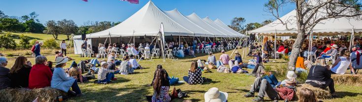 Audience sitting on grass under blue sky at Byron Writers Festival