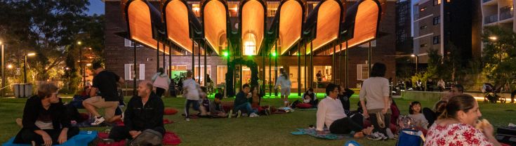 Small groups of people sitting on picnic rugs in the early evening outside of Green Square