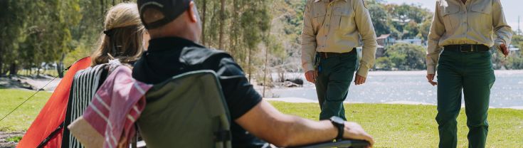 2 NPWS rangers members greeting 2  campers sitting in camping chairs