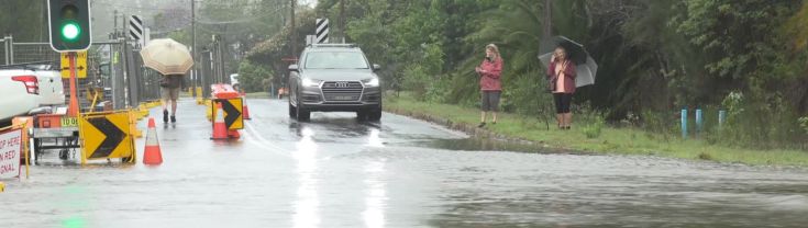  A car waits at a flooded road with emergency signage nearby.