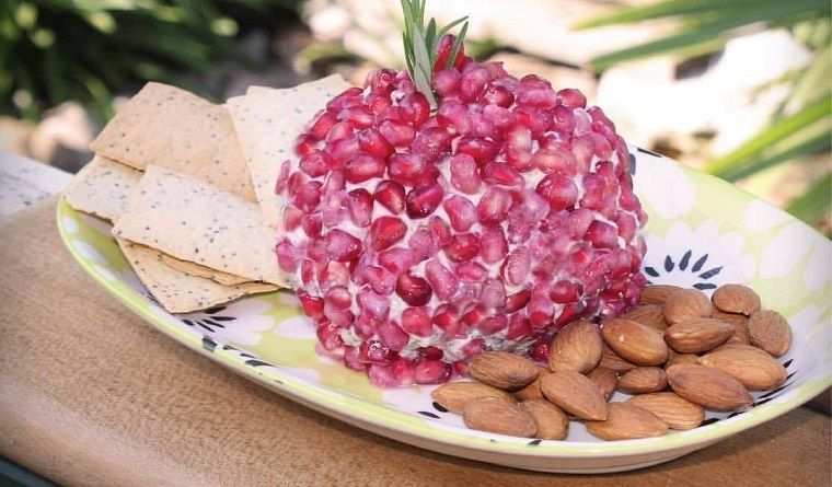 Ball of cheese on a platter, covered in pomegranate seeds