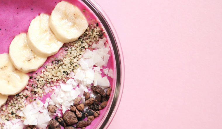 Pink bowl with sliced banana, nuts and coconut