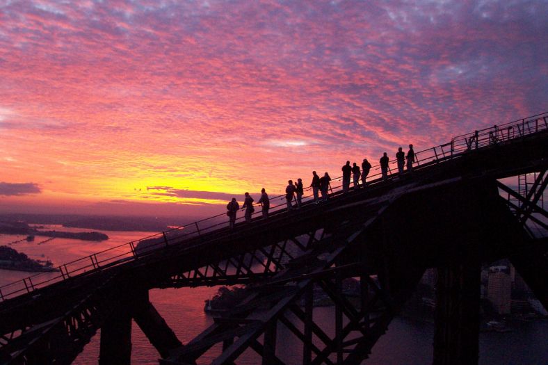 Group of people climbing the Sydney Harbour Bridge in silhouette against the twilight sunset