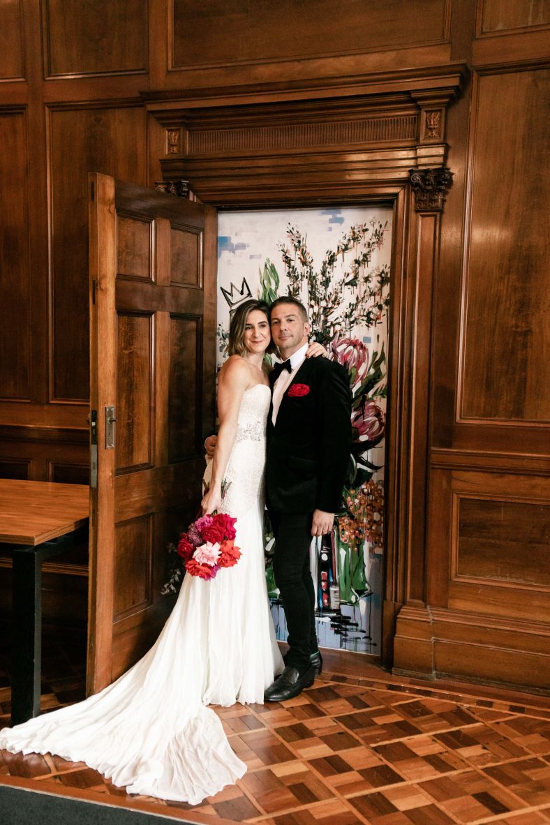 Bride and groom posing in front of a doorway revealing hidden art piece