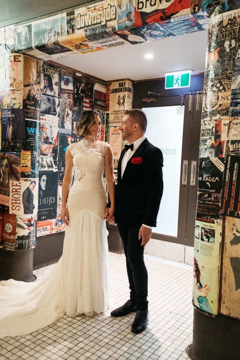 Bride and groom under an archway covered in old posters