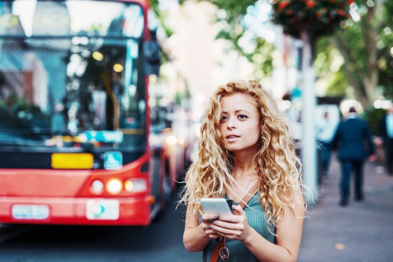 Woman looking at a phone with a bus in the background 