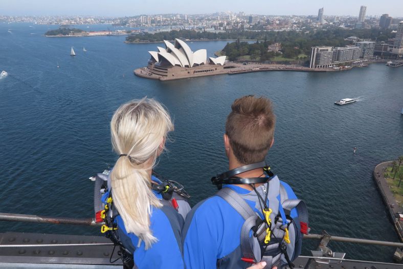 Couple climbing the Sydney Harbour Bridge over looking Sydney Opera House and harbour