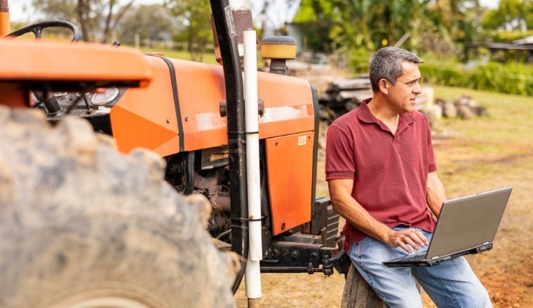 Man sitting in front of a tractor working on a laptop.