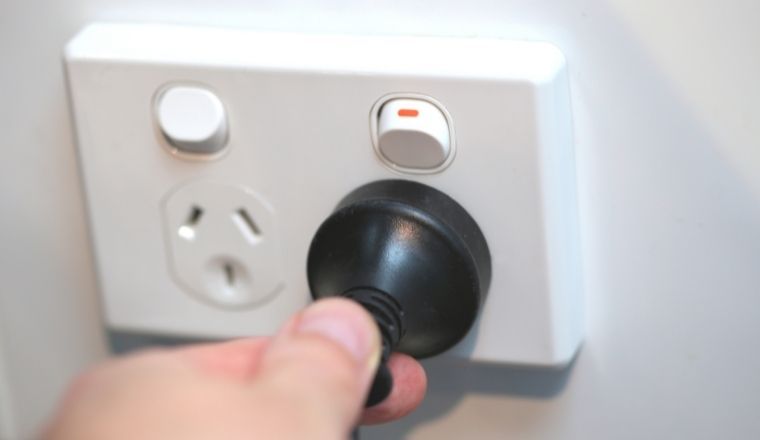 A hand placing an electric plug into a power point.