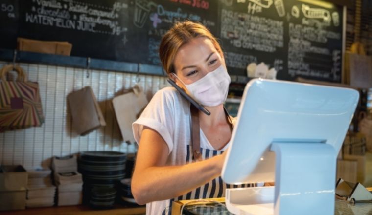 Female_small_business_owner_standing_behind_a_counter_wearing_a face_mask