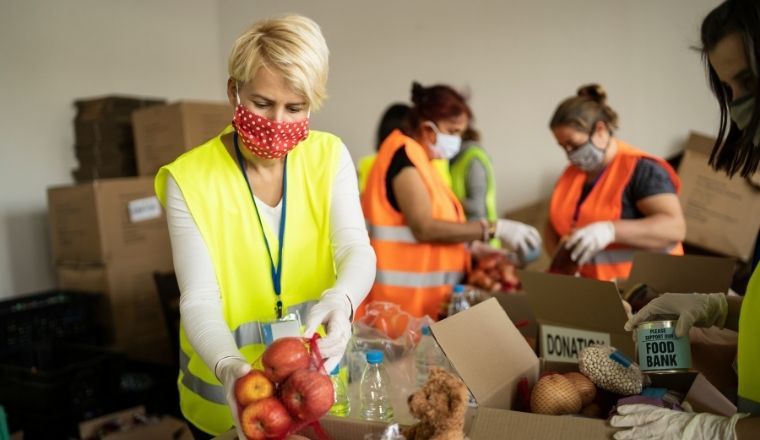 A group of people wearing protective face masks packing donated food in boxes.