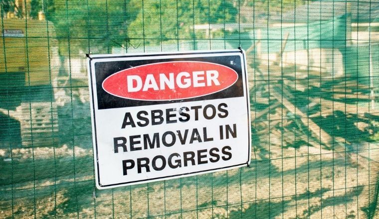 A warning sign that says Danger Asbestos on a fence at a construction site.