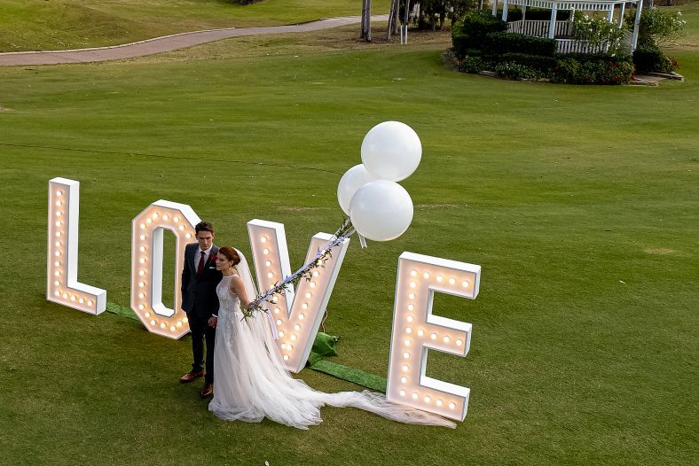 Bride and groom standing in front of a love sign.