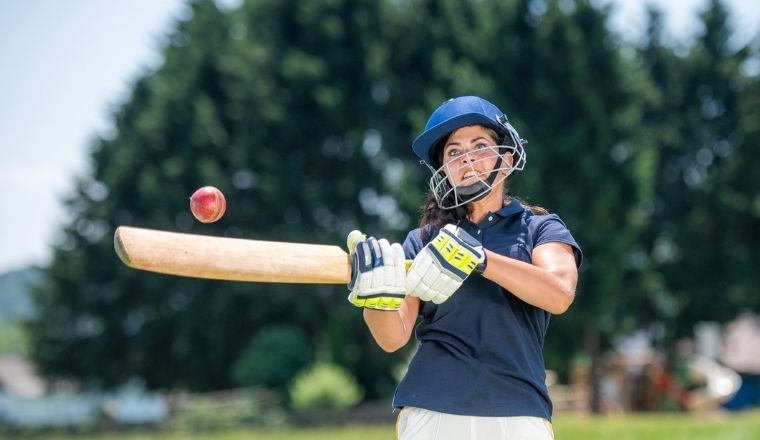 Female cricket player hitting the ball with a bat.