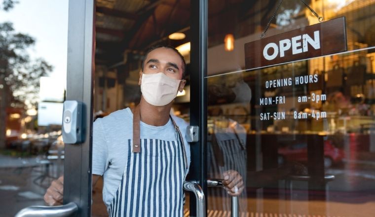 Business owner opening the door of a cafe, wearing a facemask