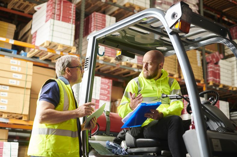 Image of a worker in a parked forklift talking to a production manager