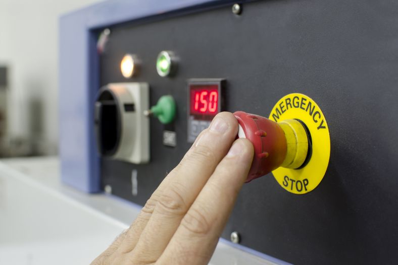 Hand pressing emergency stop button on a large manufacturing machine