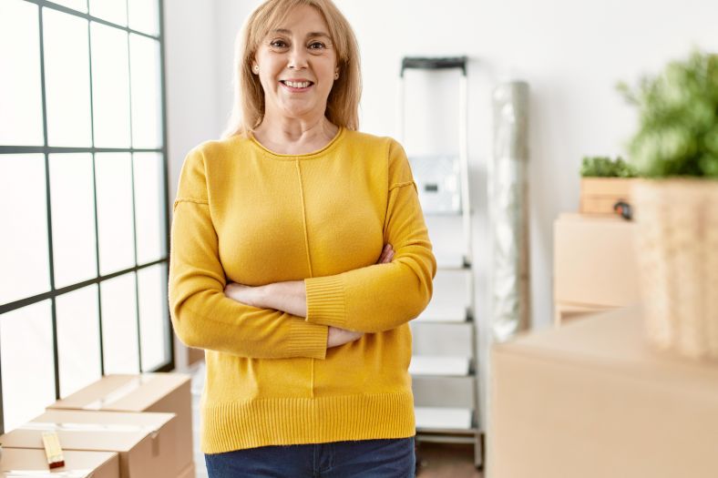Woman in yellow sweater smiling with arms crossed, with boxes in the background.
