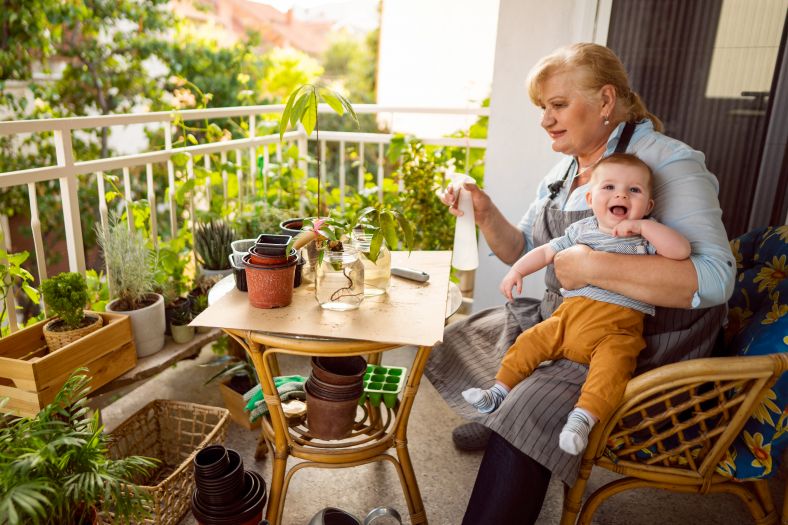 A woman holds a child while watering plants on her balcony