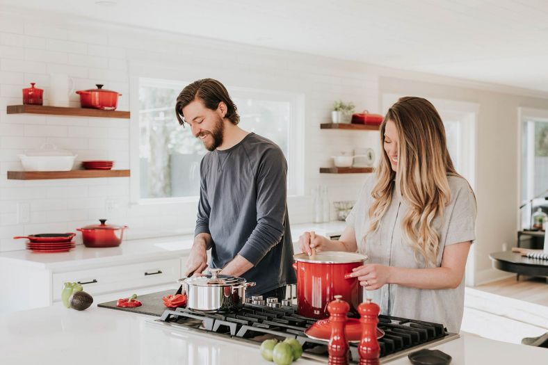 A man and woman are cooking with pots on a stove in a kitchen