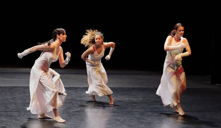 A group of three female contemporary dancers performing on stage.