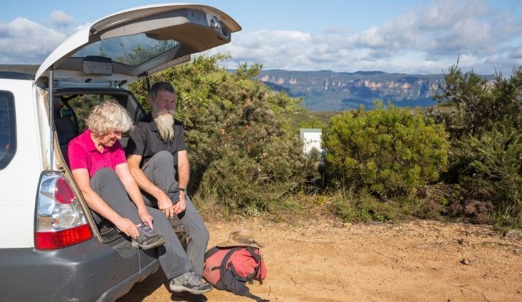Senior couple preparing to go bushwalking. Sitting in the back of a station wagon. The Blue Mountains in the background.