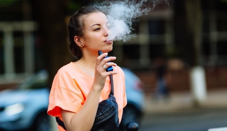 A young woman exhaling smoke vapour from an electronic cigarette.
