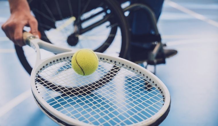 An adult man in a wheelchair playing tennis on a tennis court.