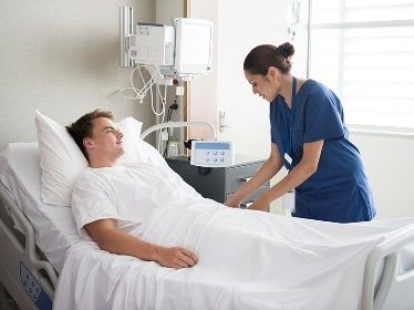 man in hospital bed with attending nurse