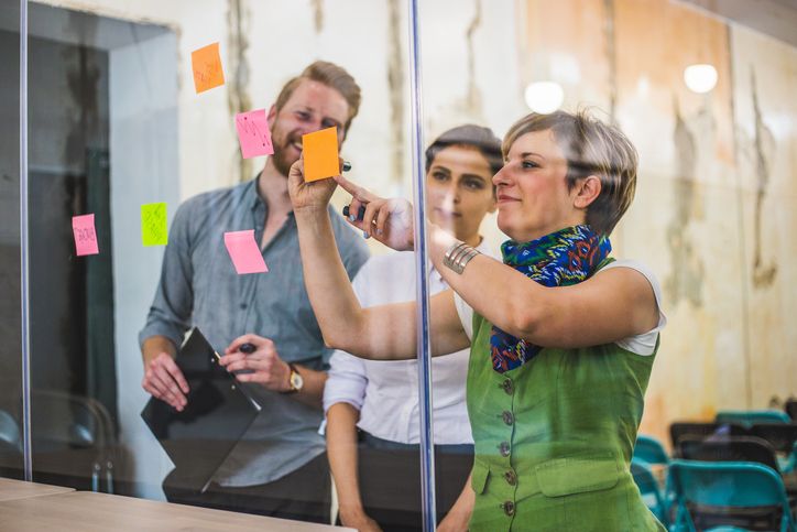 Three people discussing post-it notes on a glass window