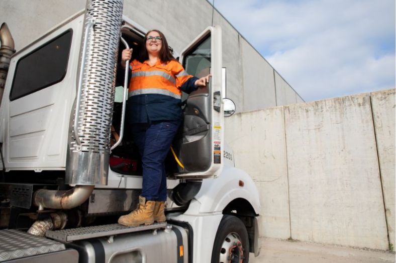 A female truck driver gets down from the cab of a large truck