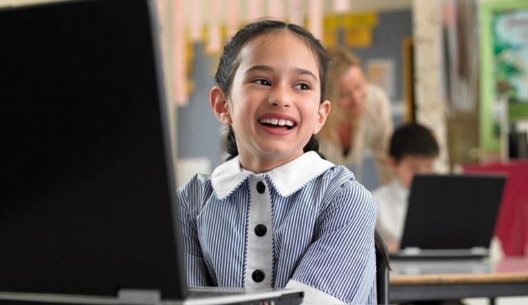 A smiling girl sitting by her laptop in a classroom. 
