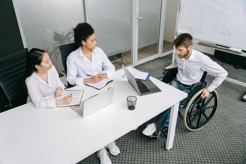 man in a wheelchair discusses work with two colleagues around a table
