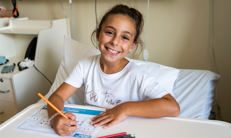 Young smiling girl sitting in hospital bed colouring in