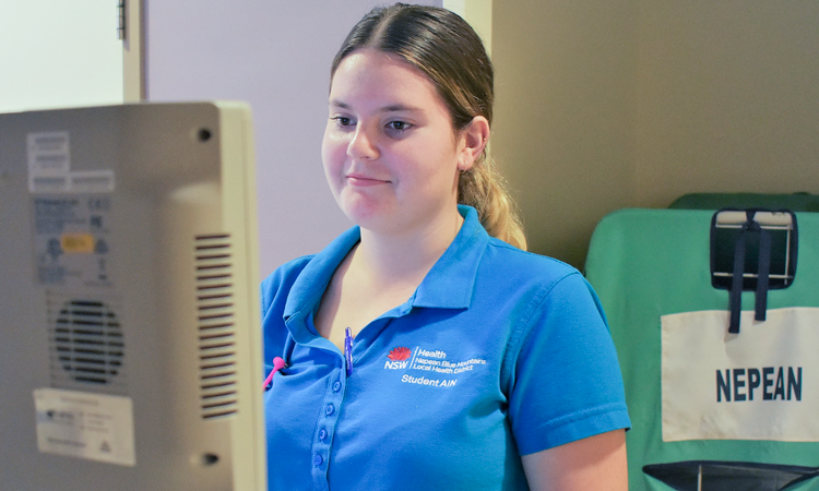 Young woman wearing NSW Health polo shirt looks at a computer screen