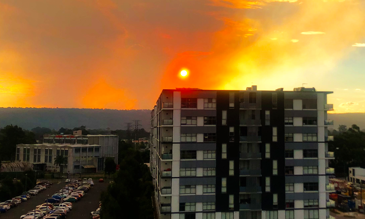 Orange sky caused by sun setting behind smog, with high rise building and cars in carpark in foreground