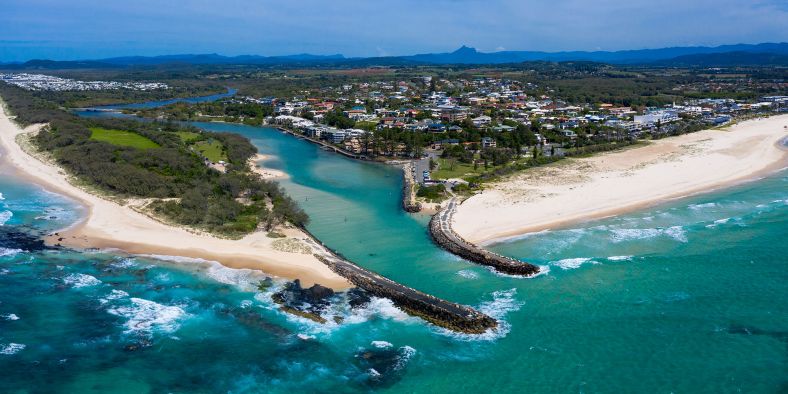 An aerial photo over a coastal town next to a river and two sandy white beaches 