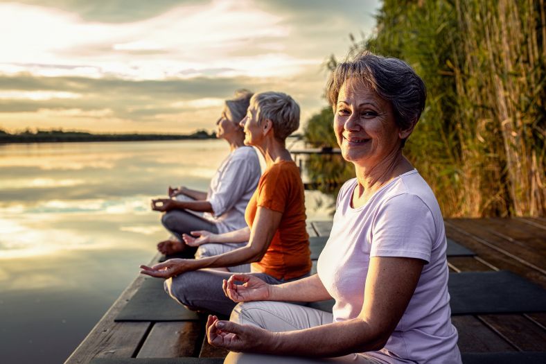 Three women are staring out over a lake doing yoga at sunrise.