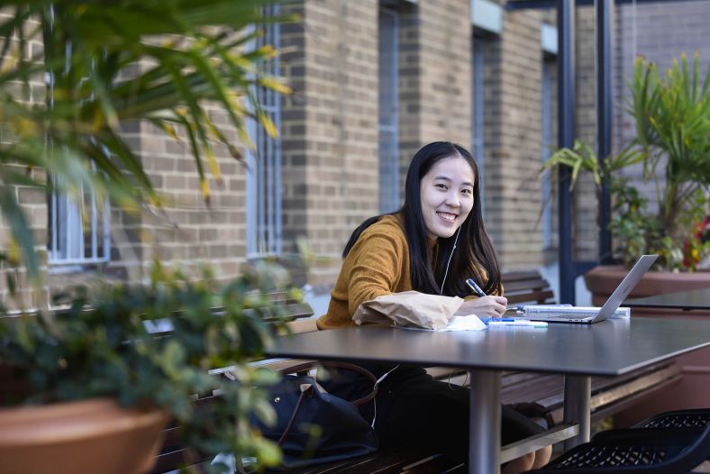 Young student studying outdoors. She is smiling at the camera