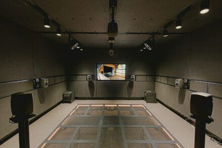 Image of a room with a screen and multiple speakers pointing towards the centre of the room 