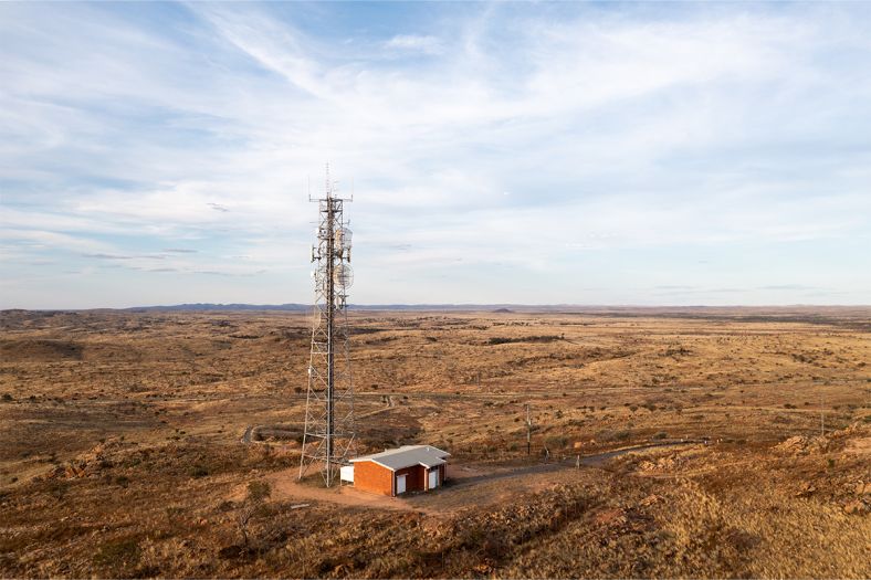An aerial view of a mobile tower in the middle of a paddock against a blue sky with some clouds