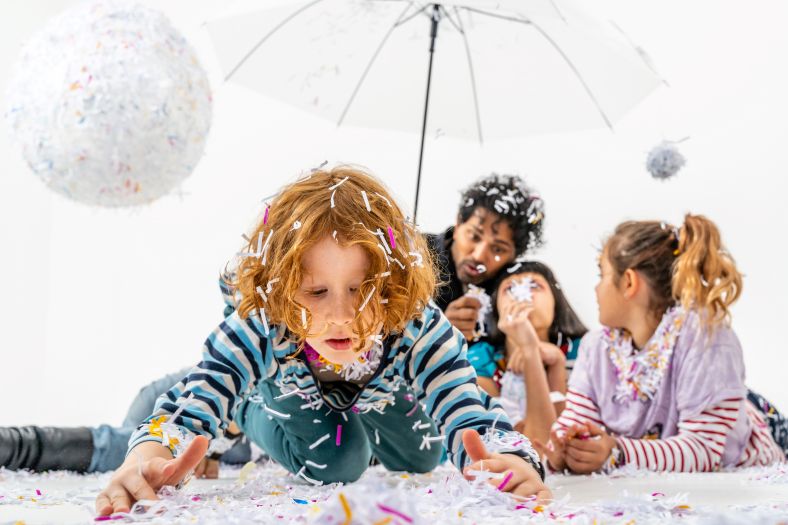 Photo of children playing in a space covered in confetti and shredded paper