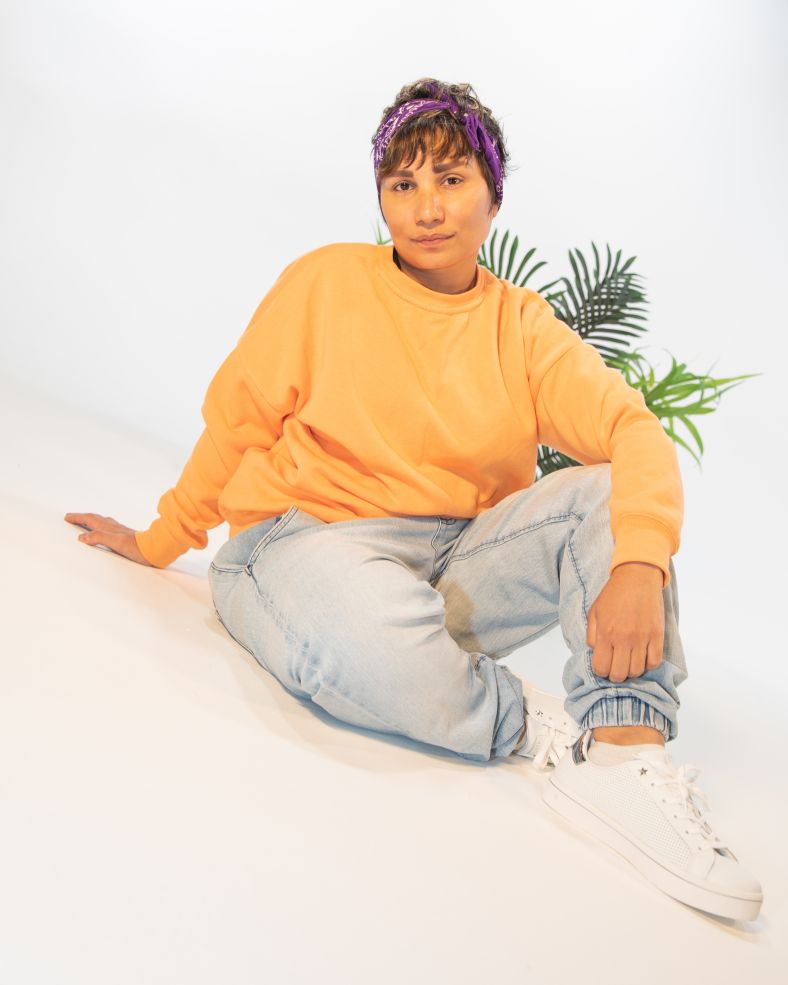 Image of Thalia Skopellos, sitting on the ground in a yellow jumper and jeans