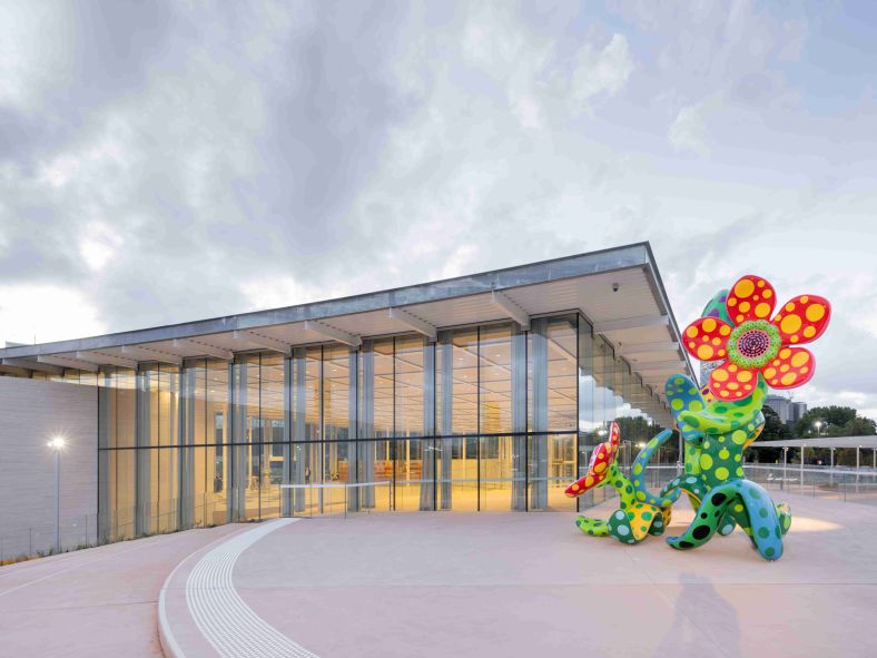 Large artistic flower sculpture beside modern glass framed building