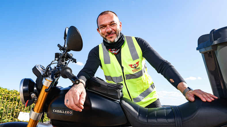 A smiling man standing beside his motorcycle