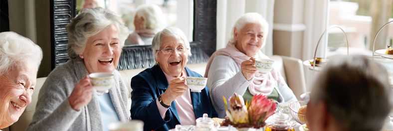 Group of senior ladies smiling and laughing while drinking tea
