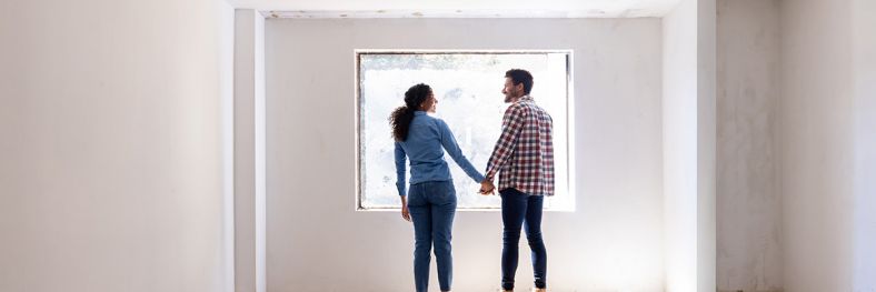 two people standing holding hands looking out the window of an empty apartment