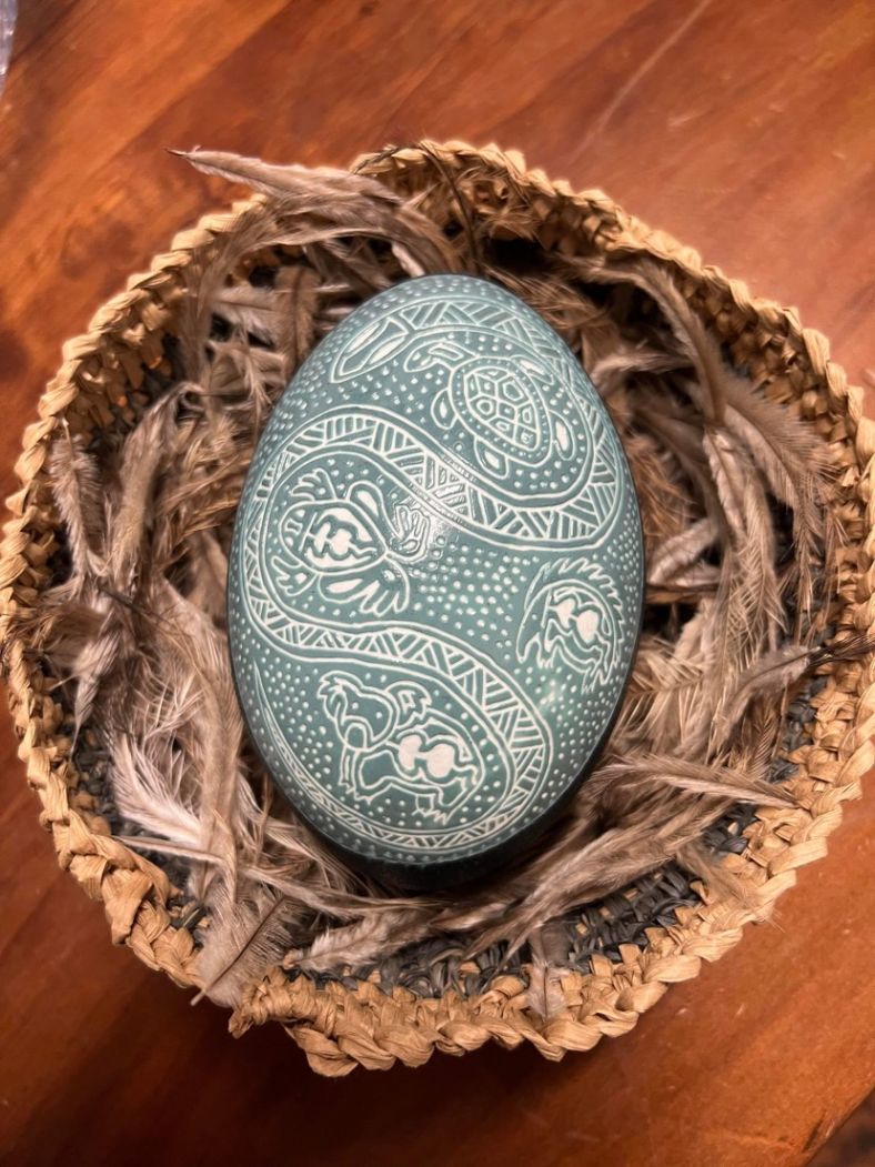 Emu egg carved with designs of animals, turtle, koala, frog and echidna in a hand woven basket